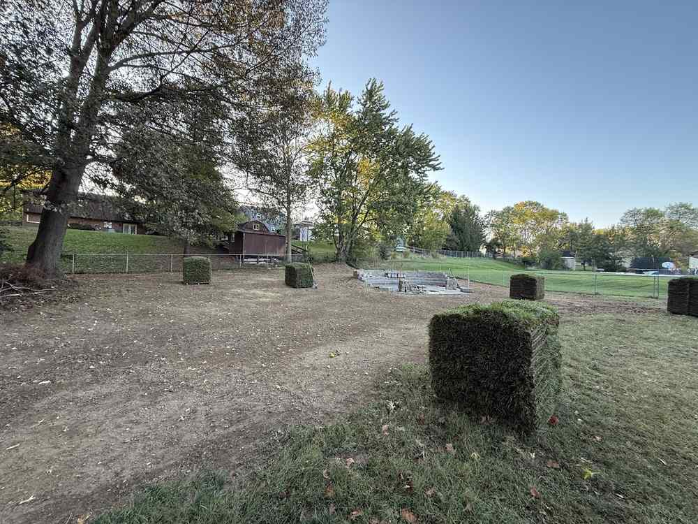 A back yard cleared to bare dirt, with pallets of sod waiting and a half-built stone wall in the distance.