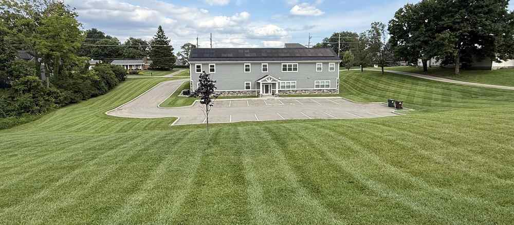 A wide lawn mowed in long stripes in front of a two-storey commercial building.